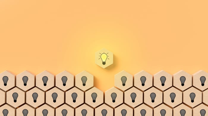 Lightbulbs illustrated on wooden blocks with one shining yellow bulb above the rest. 