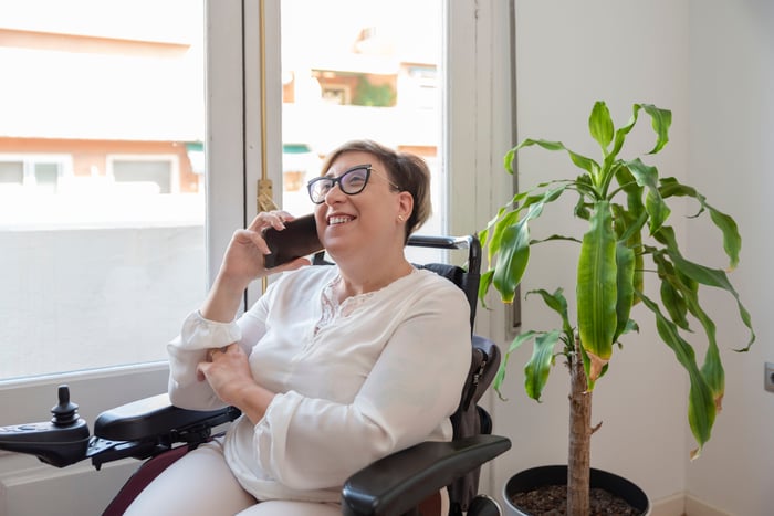 Someone seated next to a plant is on the phone, smiling.