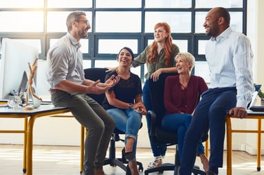 A team of five employees laughing while talking in the office