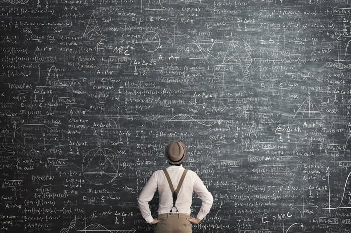 Person solving a complex math problem on a large blackboard.