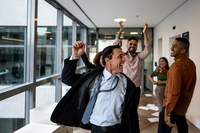 Some people in an office hallway are raising arms in celebration.
