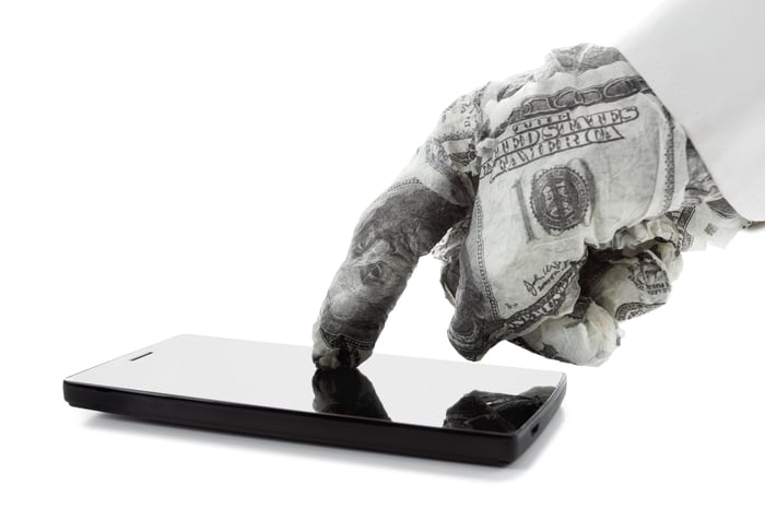 A hand wrapped in cash touching a smartphone.