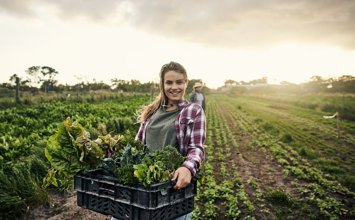 A woman in a field with a grey shirt holding vegetables. 