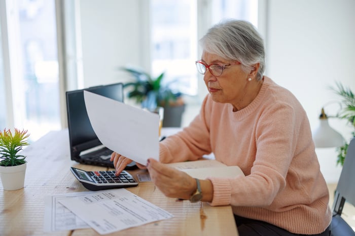 A person sits at a desk in front of a laptop to review paperwork.