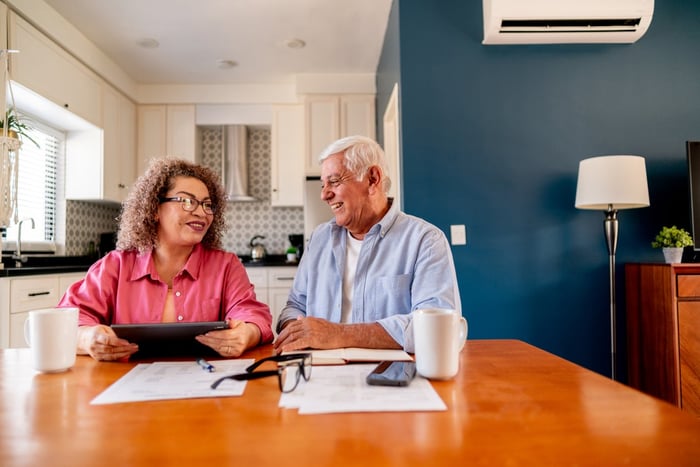 A retirement-age couple smiling as they look through documents at their kitchen table.