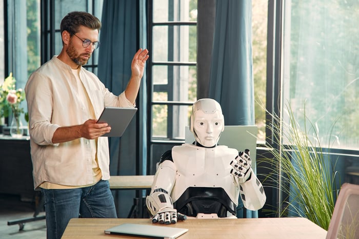 A person reads aloud from a tablet as a robot looks on.