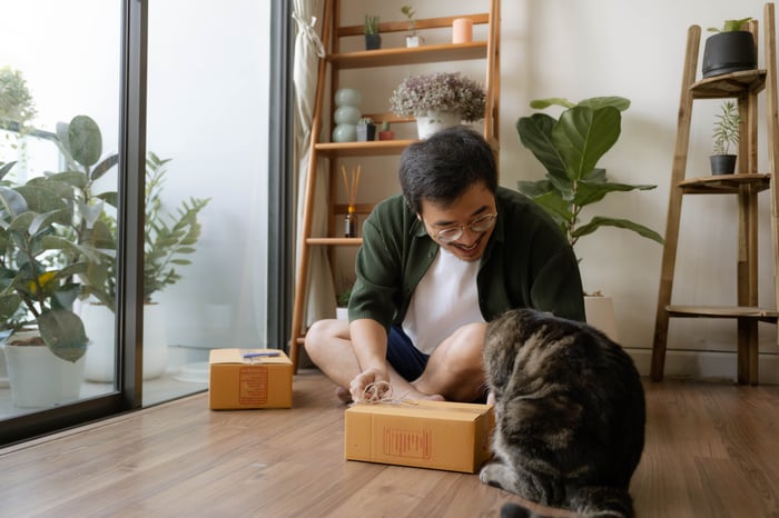 A man sits on the floor and looks at his cat. He is happy. 