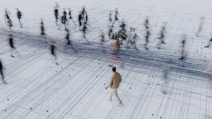 A person walking alone among blurred human figures on a surface marked by parallel and circular lines with an array of dots. 