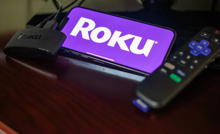 Roku's logo is displayed on a mobile phone next to a TV remote. 