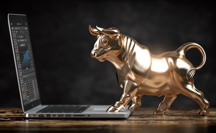 A golden bull stands on a computer keyboard; stock prices are displayed on the screen.