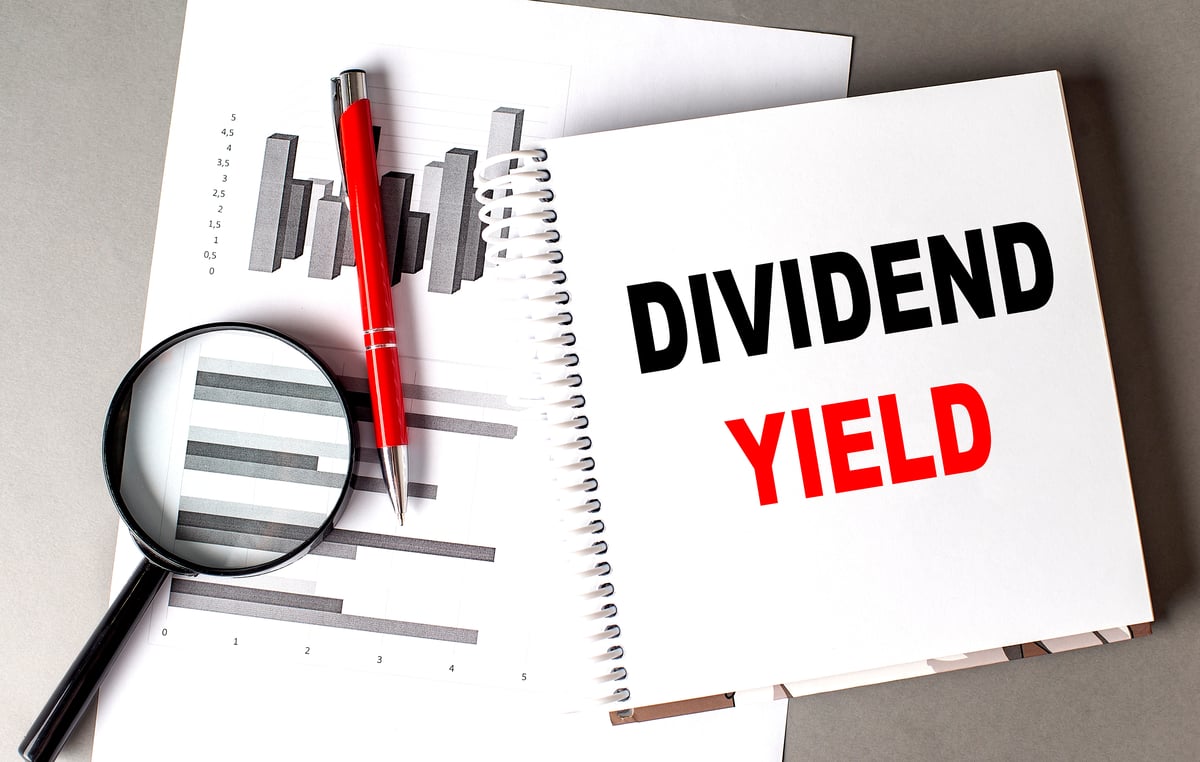 dividend yield written on notebook next to charts, pen, and magnifying glass