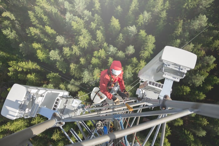 A worker and a wireless network model atop a tall cell tower.