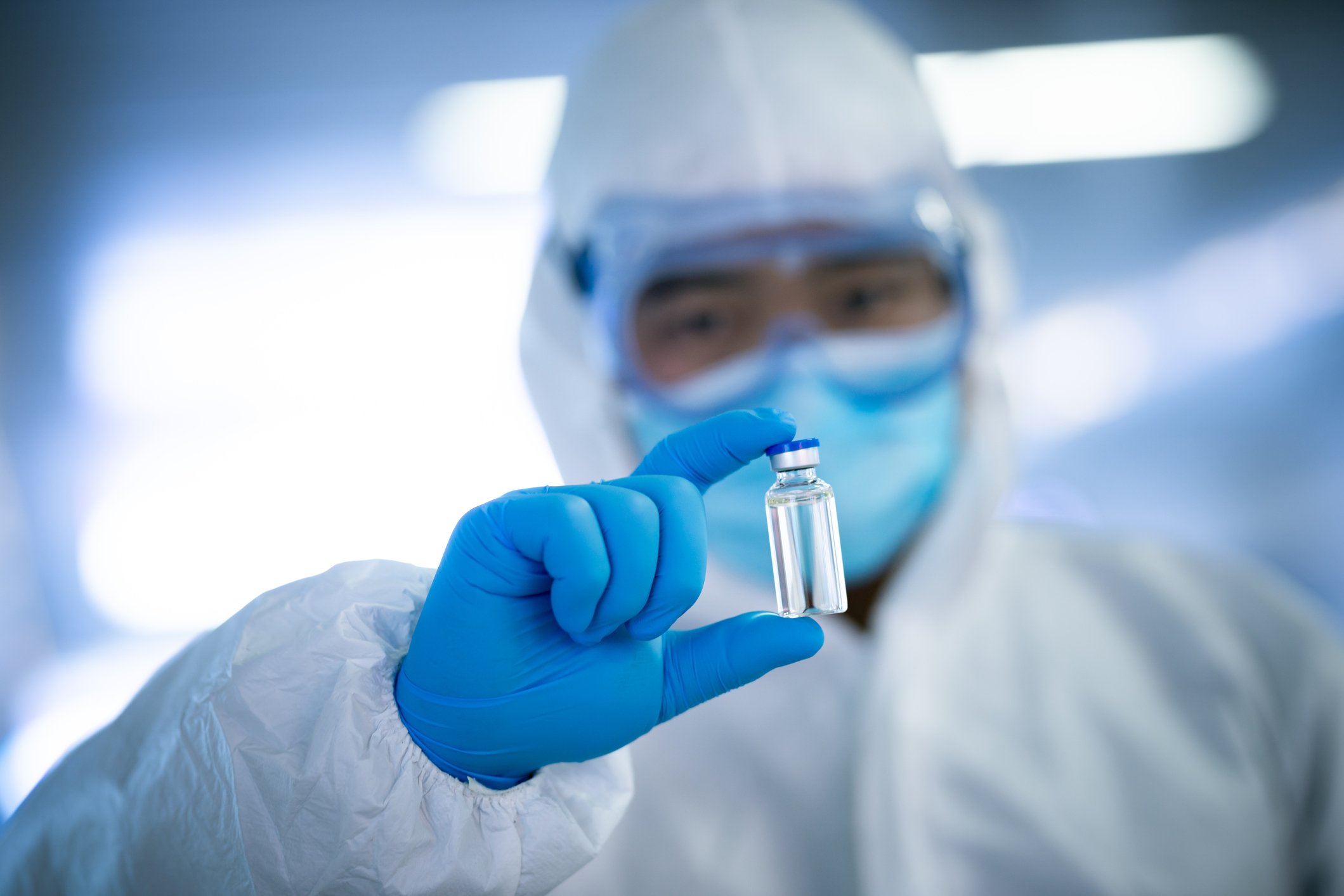 Chinese doctor in clean suit examining a capped bottle of vaccine