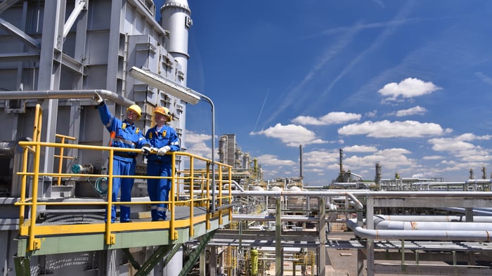 Two people standing at an oil refinery.