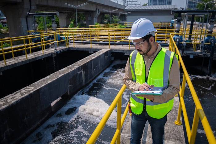 A working in a heard hat with a clipboard at a water treatment plant.