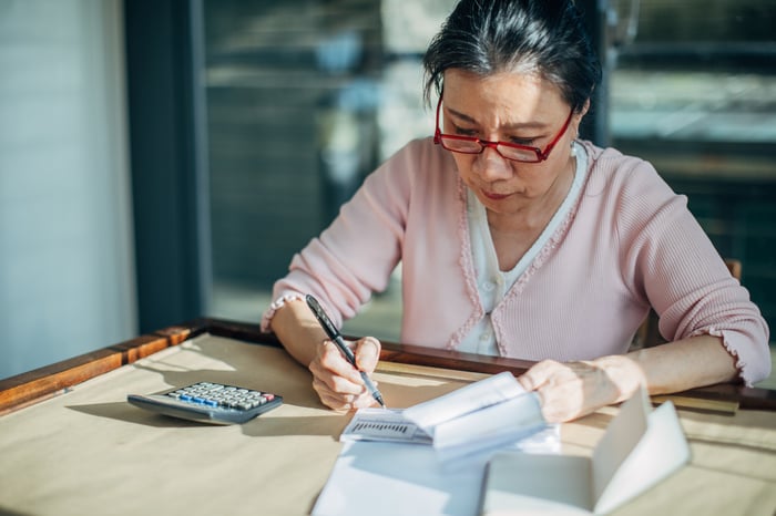 Person sitting at desk with pen, paper, and a calculator.