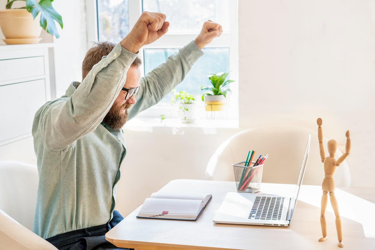 investor looks at laptop and raises arms in celebration.