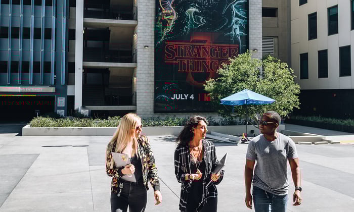 Three people walking away from a Stranger Things banner.