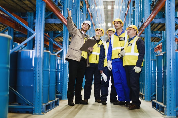 Group of people conversing in a facility full of oil barrels.