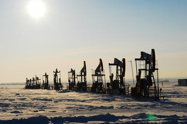 A row of oil pumpjack silhouettes in a barren landscape.