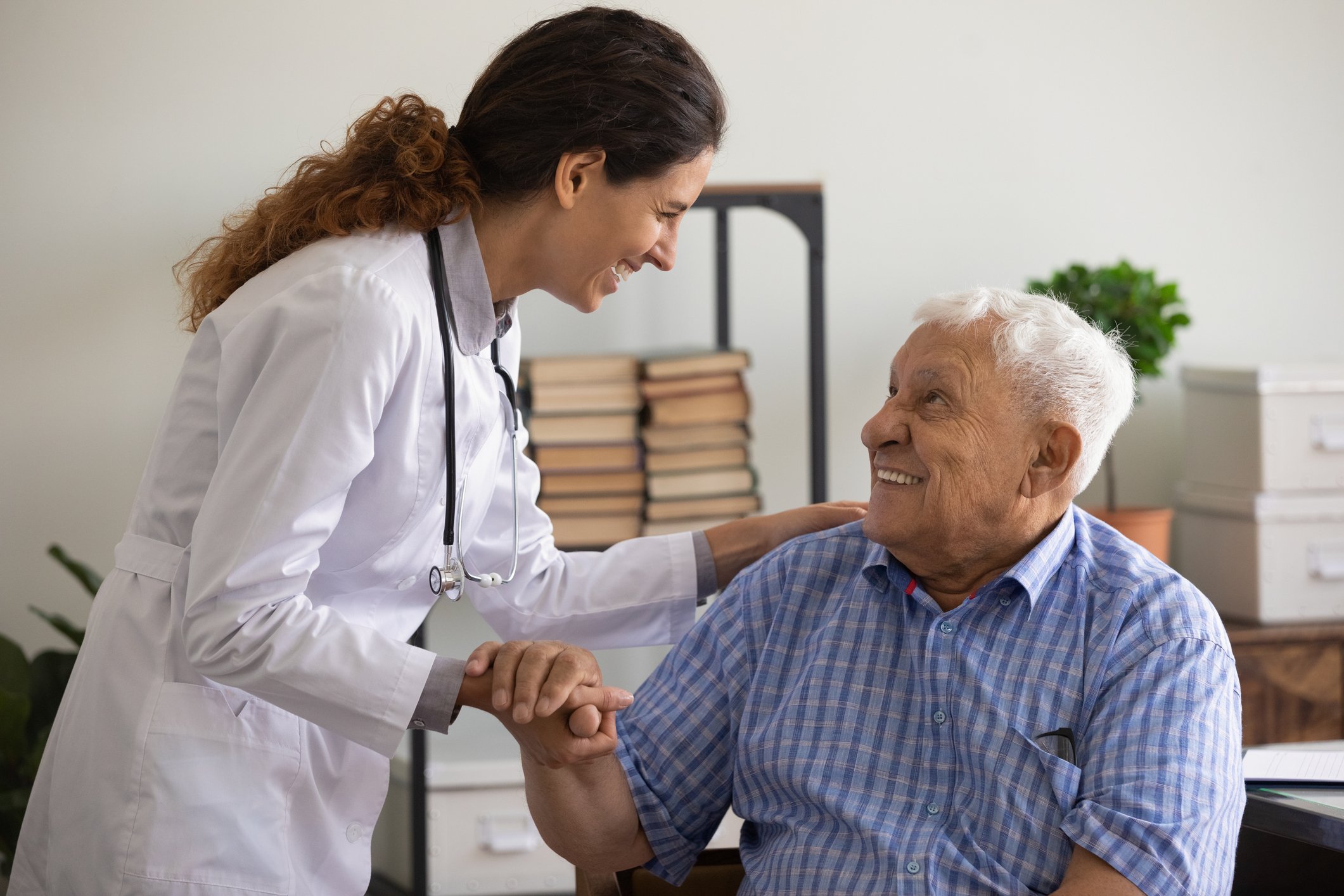 A doctor leans over and holds patient's hand while patting their shoulder_GettyImages-1319103349