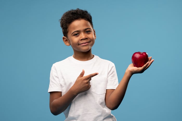 Little boy pointing at a red apple and smiling.
