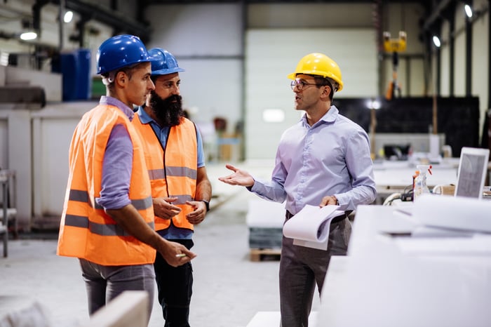 Three workers with hard hats in a factory hall. 