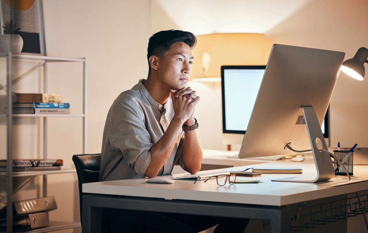 An investor clasps their hands while sitting at a desk in front of a monitor.