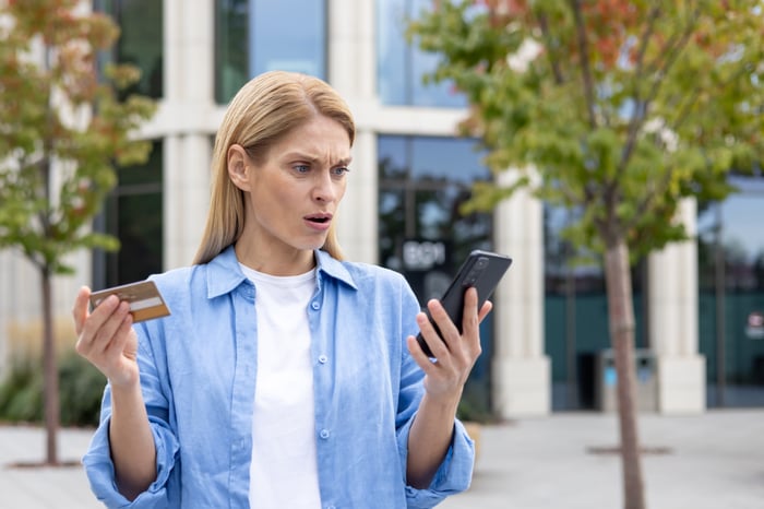 a woman looking confused at her phone and credit card in each hand. 
