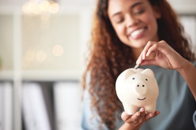 Person stuffing money into a piggy bank and smiling