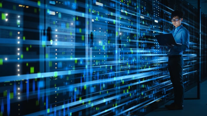 A person holding a laptop while standing in front of data servers.