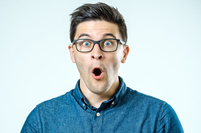 Person in a blue shirt and glasses looking amazed, with mouth open.