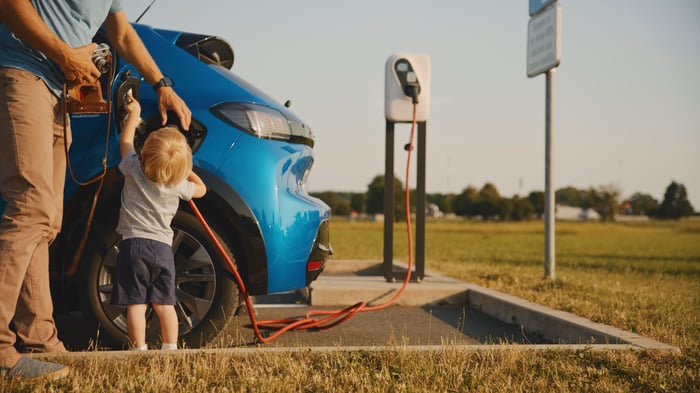 A child helps their parent plug in their electric vehicle.
