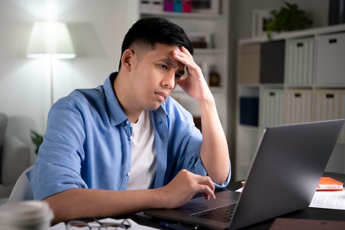 A person looks upset while viewing a laptop.