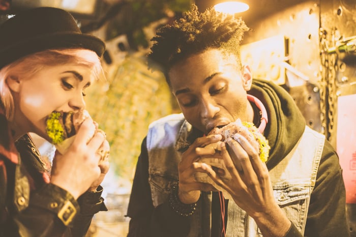 Two people are eating chicken sandwiches at a restaurant. 