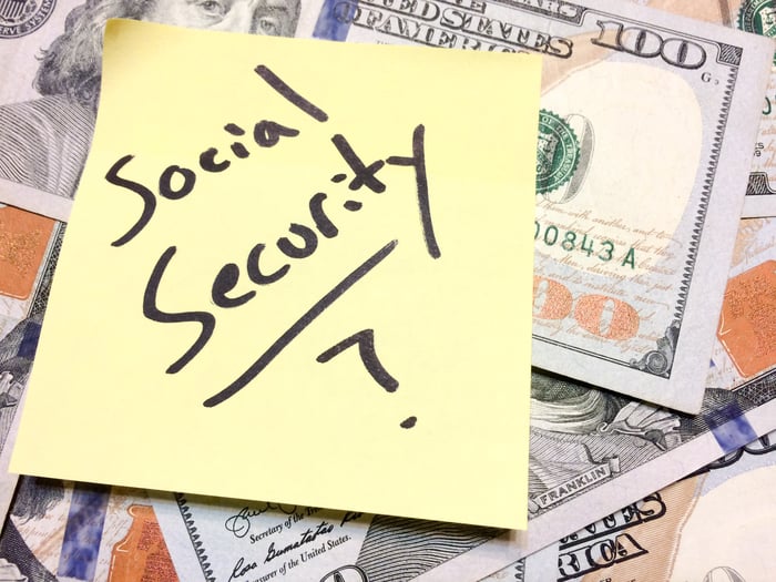 A sticky note with "Social Security?" written on it on top of $100 bills.