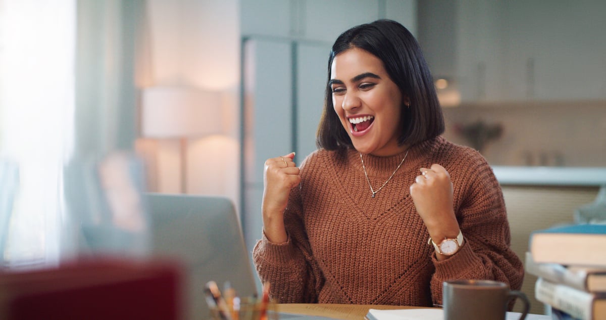An investor smiles as they sit at a desk in front of a laptop.