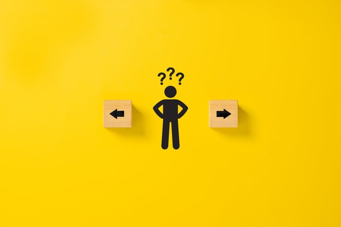 A nondescript figure faced with choosing between 2 opposite directions represented by arrows on blocks. 