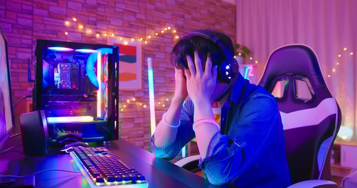Man with hands over his face in front of desktop wearing headphones. 