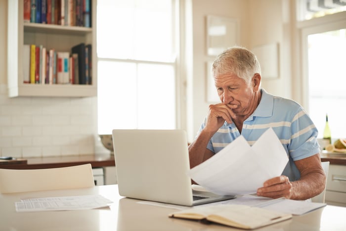 A person at a laptop  holding papers.