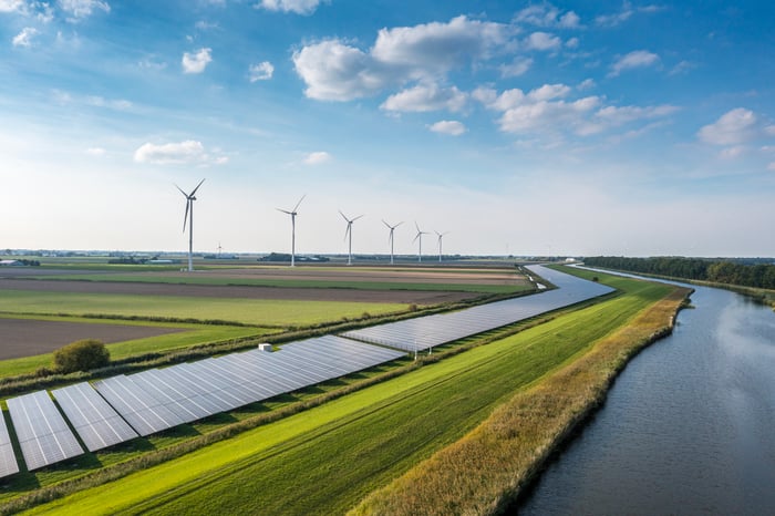 Solar panels and wind turbines near a river.