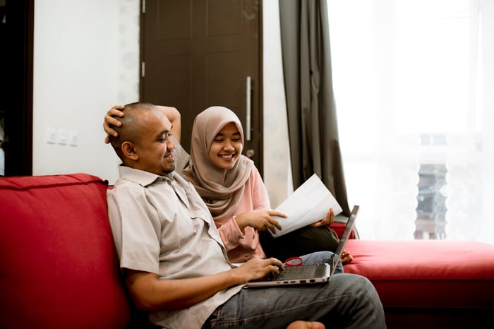 Two people smiling at a shared tablet computer on the couch.