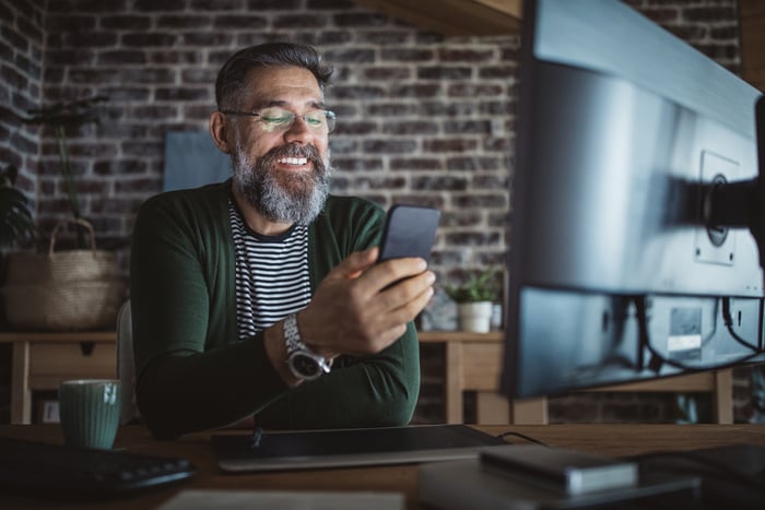 A person is smiling while looking at a smartphone. 