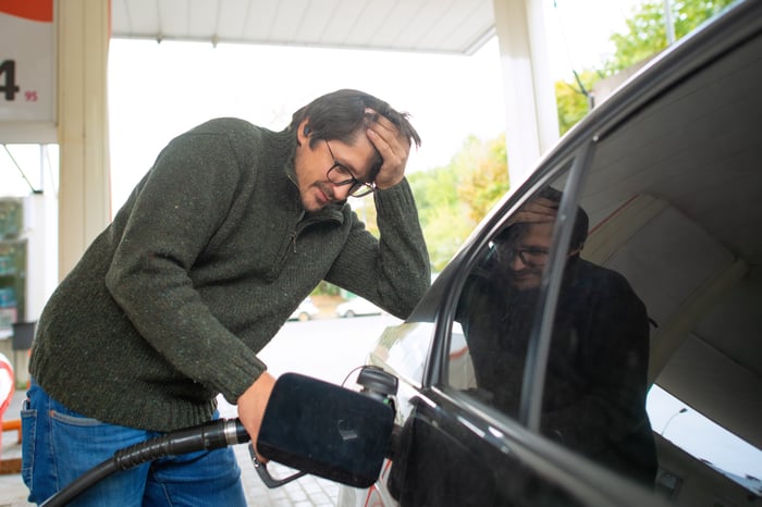 A man with hand on head as he fills his gas tank.