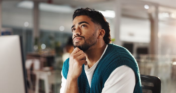 A person looking up, thinking, while at desk. 