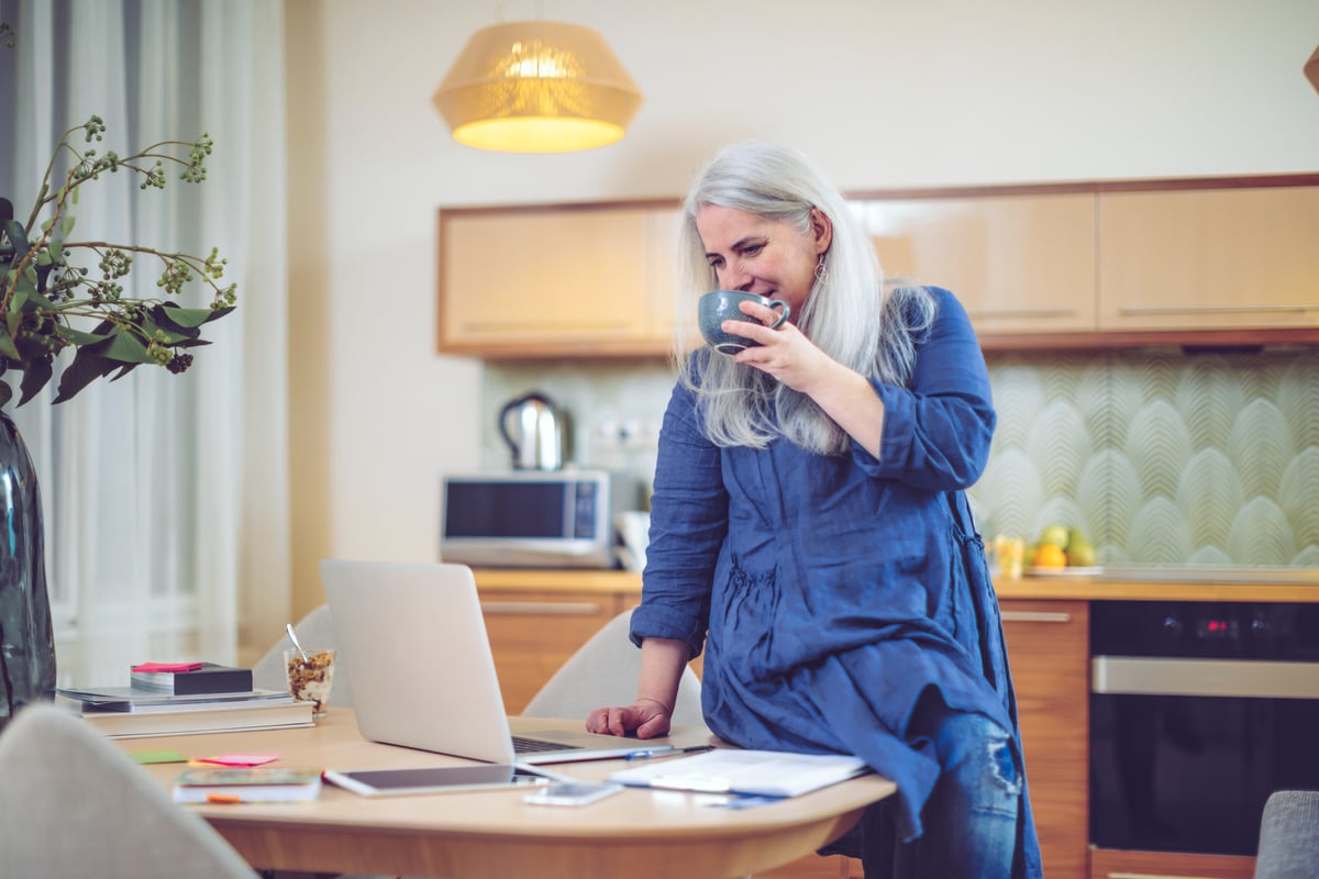 Smiling person drinking from mug and checking laptop