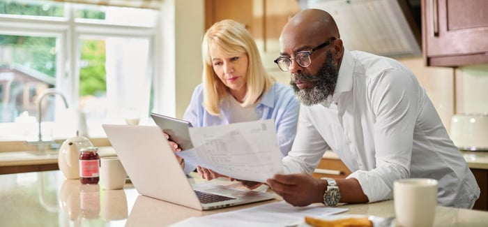 Older couple leaning on kitchen island, looking over paperwork. 