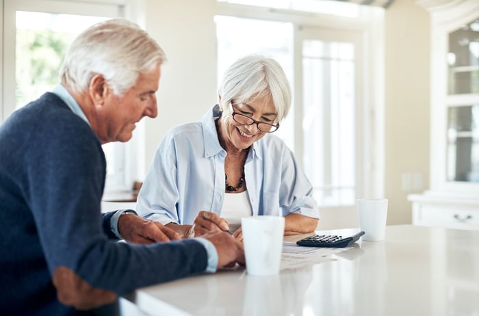 Two investors sit at a kitchen table with a calculator and some documents which they are reviewing.