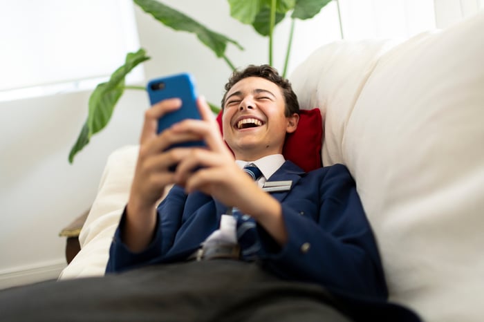 A young person on a sofa holding their phone and laughing.