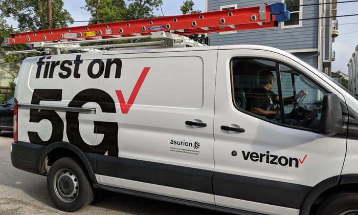 A white Verizon van with a ladder on the roof.